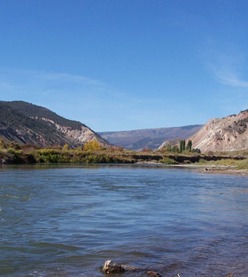 Clear river flowing through a valley, flanked by mountains and autumn foliage under a blue sky